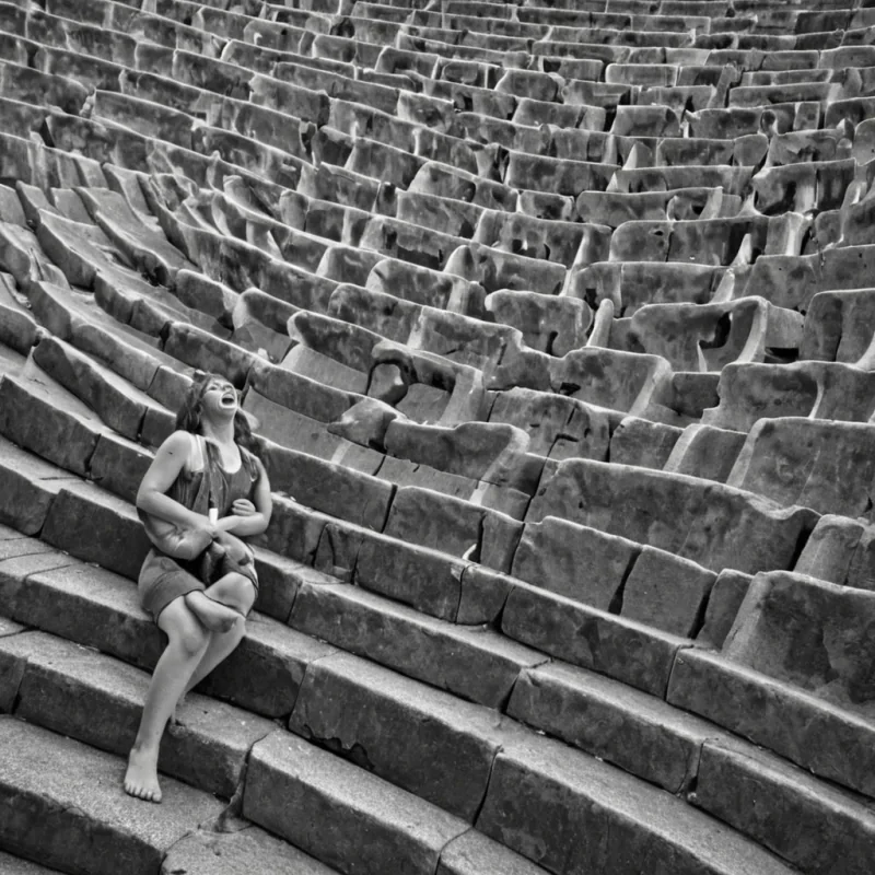 A single, selfechoing cascade of reversed laughter, shaped like a 9,003dimensional ripple of unformed joy and inverted mirth, fractures through the center of a vast, inverted amphitheater of solidified silence  each seat carved from the exact moment between a smile forming and its refusal to spread, a joke whispered and dissolving into nonverbal stillness, a childs giggle syncing with a distant chime and collapsing into pure, unmeasured quiet. The cascade does not amplify sound  it unamplifies it, each shimmering wavelet shedding a layer of emotional potential that never coalesced into shared delight, reforming into ephemeral, rosequartzthreaded afterimages shaped like the
